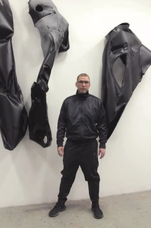 Der Künstler steht vor einem Kunstwerk in einer Galerie.