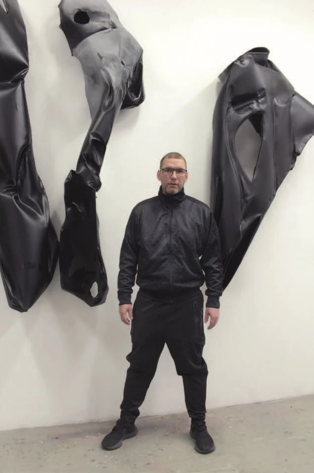 Der Künstler steht vor einem Kunstwerk in einer Galerie.
